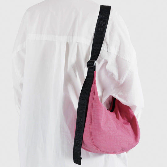 The Medium Crescent Bag in Azalea Pink from Baggu is a stylish and versatile accessory that can complement any outfit. It is made of durable nylon and features a zippered main compartment, an interior slip pocket, and an adjustable shoulder strap.