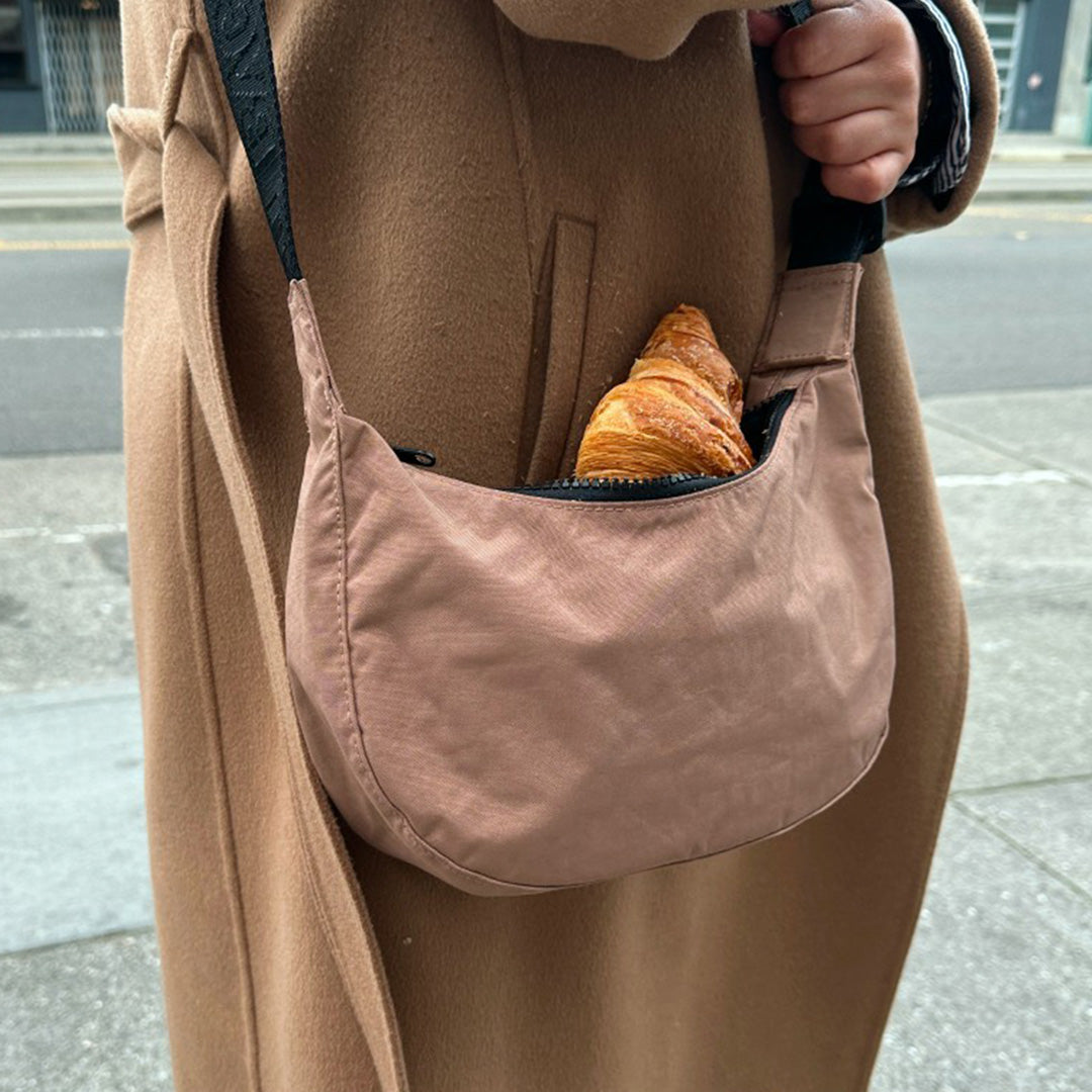 The Medium Crescent Bag in Cocoa from Baggu is a stylish and versatile accessory that can complement any outfit. It is made of durable nylon and features a zippered main compartment - lifestyle