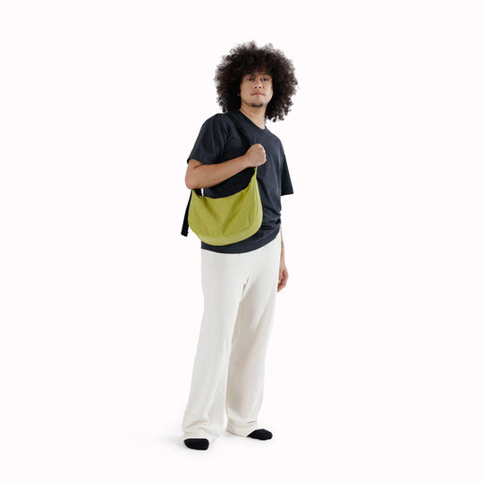 The Medium Crescent Bag in Lemongrass from Baggu is a stylish and versatile accessory that can complement any outfit. It is made of durable nylon and features a zippered main compartment, an interior slip pocket - as worn by model