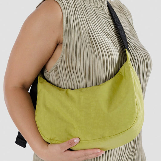 The Medium Crescent Bag in Lemongrass from Baggu is a stylish and versatile accessory that can complement any outfit. It is made of durable nylon and features a zippered main compartment, an interior slip pocket - as worn detail