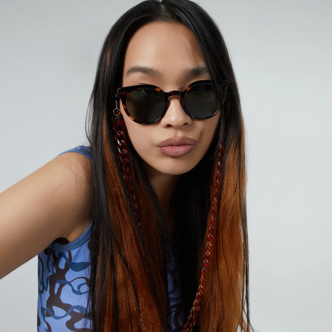 The Lulu as worn by model featuring a unique combination of round lenses set in a cat-eye frame. The Lulu Crystal Giraffe offers unparalleled style and protection with a 133mm x 49.4mm Bio Nylon frame, 100% UV400 lenses, and scratch-resistant PC lens. These gorgeous sunglasses feature a giraffe patterned light and dark brown Bio Nylon frame with solid dark green lenses. Quirky, chic, cool.