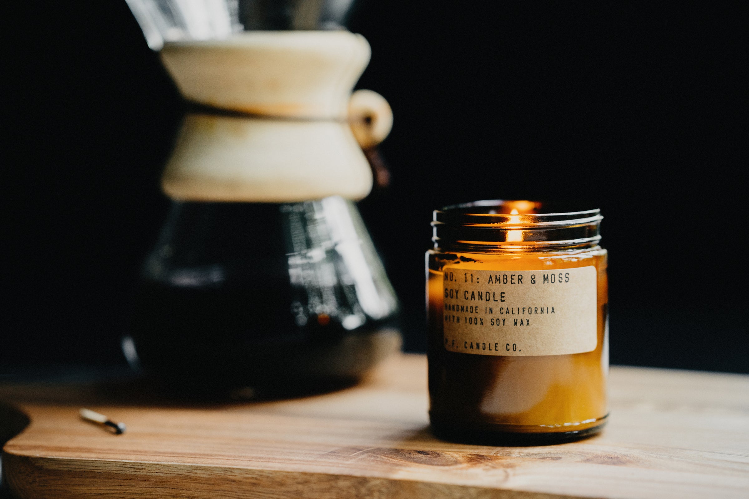 A lit PF Candle Co Classic Line Amber & Moss Candle with flame