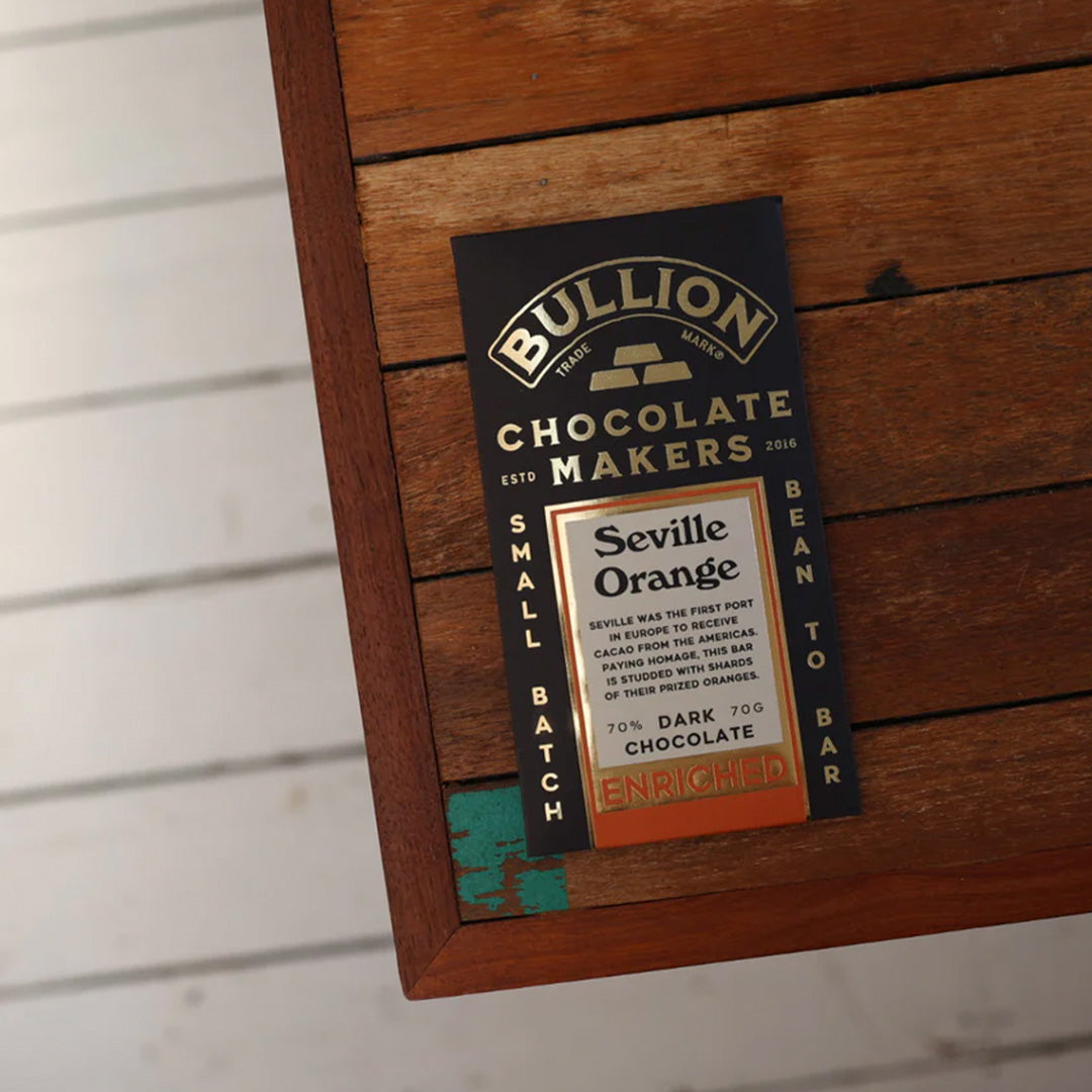 Seville was the first port in Europe to receive cacao from the Americas. Paying homage, this bar from Bullion Chocolate is studded with shards of their prized oranges.. shown on table.