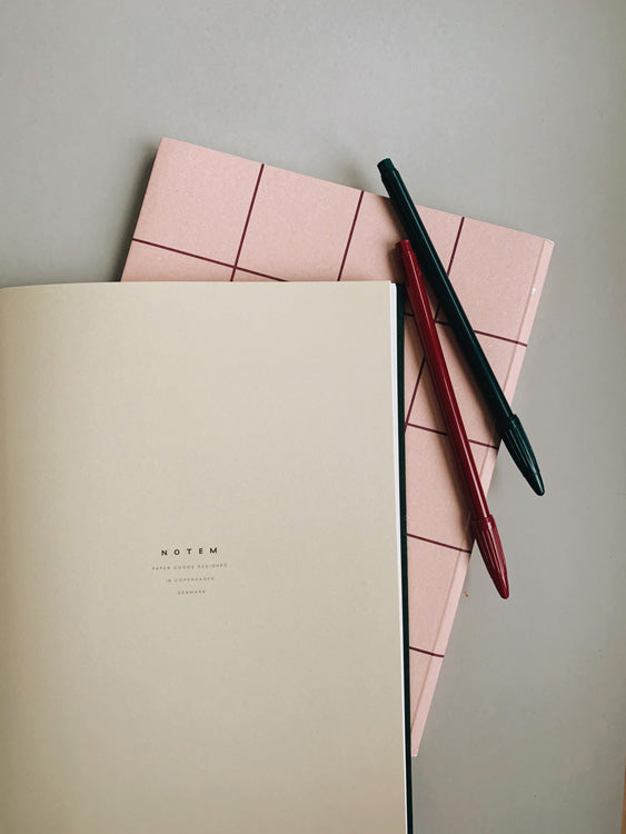 Notem Stationery, Danish Stationery brand. 2 pens on pink notepad resting on table, liferstyle image
