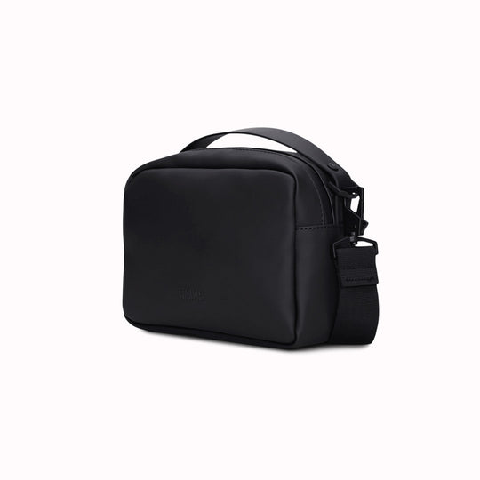 The Rains Box Bag in black is a sleek and minimalist bag crafted from Rains' signature waterproof PU fabric. It features a boxy silhouette with clean lines and a single main compartment secured by a coated zip closure.