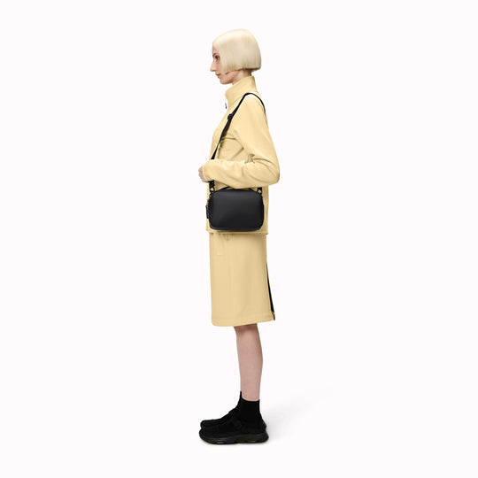 The Rains Box Bag in black is a sleek and minimalist bag crafted from Rains' signature waterproof PU fabric. It features a boxy silhouette with clean lines and a single main compartment secured by a coated zip closure.