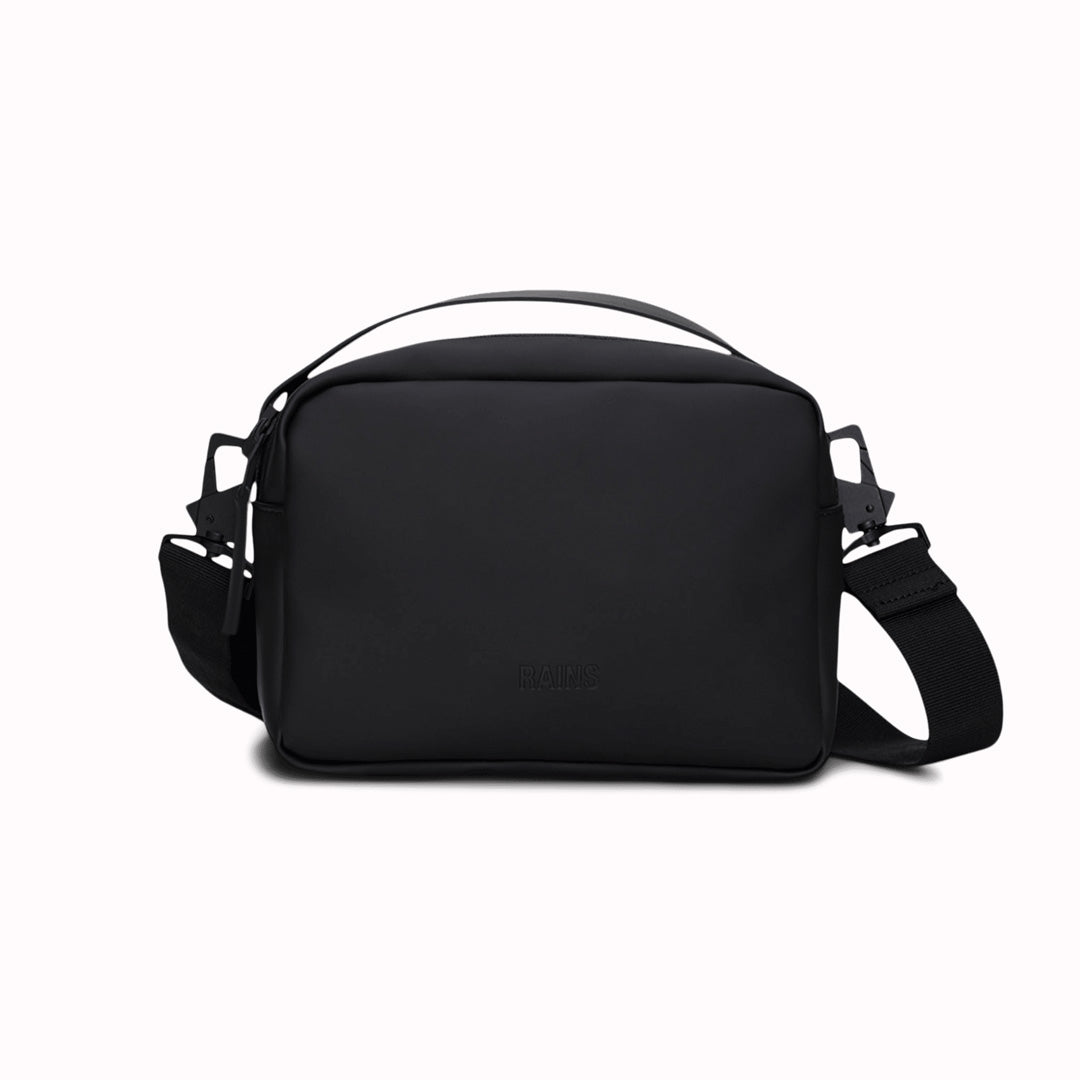 The Rains Box Bag in black is a sleek and minimalist bag crafted from Rains' signature waterproof PU fabric. It features a boxy silhouette with clean lines and a single main compartment secured by a coated zip closure.