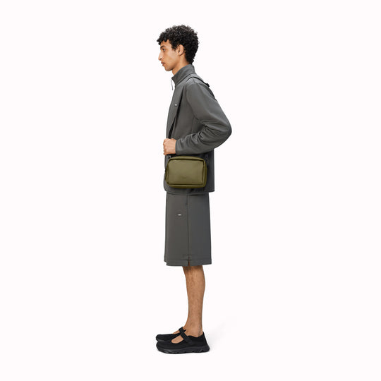 The Rains Box Bag in green is a sleek and minimalist bag crafted from Rains' signature waterproof PU fabric. It features a boxy silhouette with clean lines and a single main compartment secured by a coated zip closure.