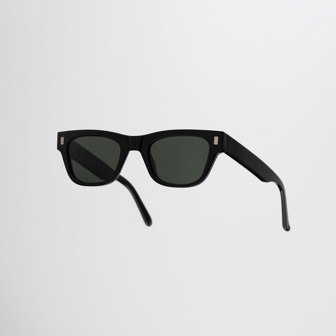 Monokel Aki Sunglasses in Black with a solid green lens sits low on the bridge with a slim, rectangular profile that keeps things sharp