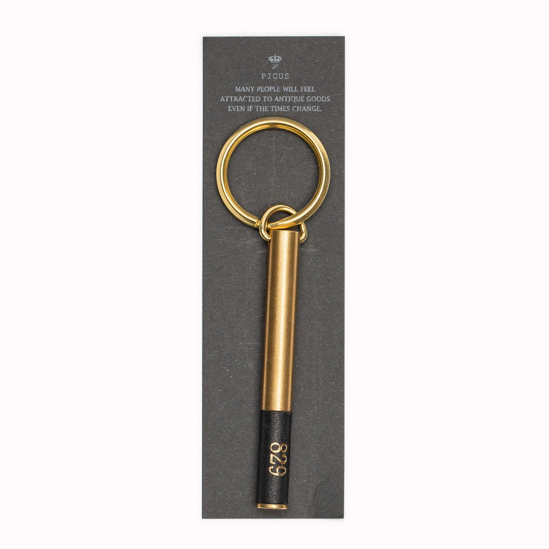 Display Card. Brass cylindrical keyring from Japanese brand Picus. These small but weighty keychains have been designed to resemble upmarket hotel key fobs and are made from solid brass with a black leather decorative end.