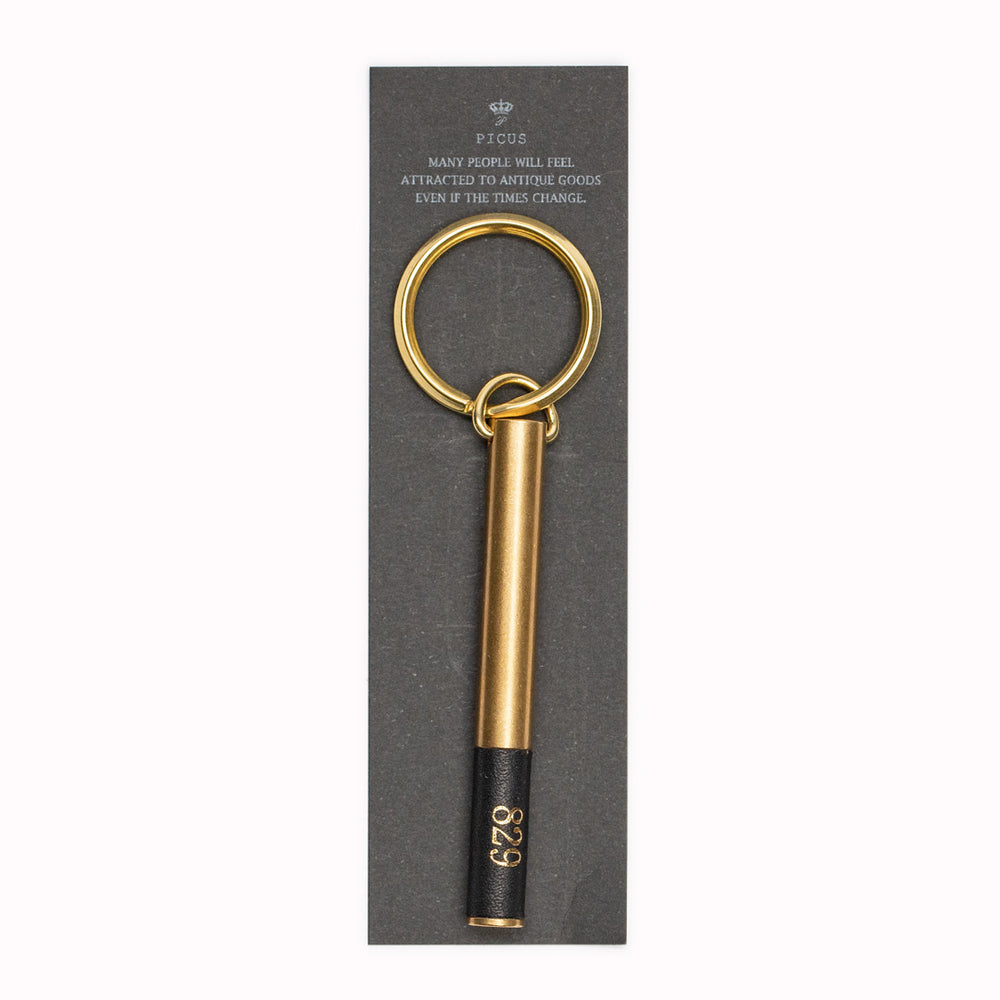 Display Card. Brass cylindrical keyring from Japanese brand Picus. These small but weighty keychains have been designed to resemble upmarket hotel key fobs and are made from solid brass with a black leather decorative end.