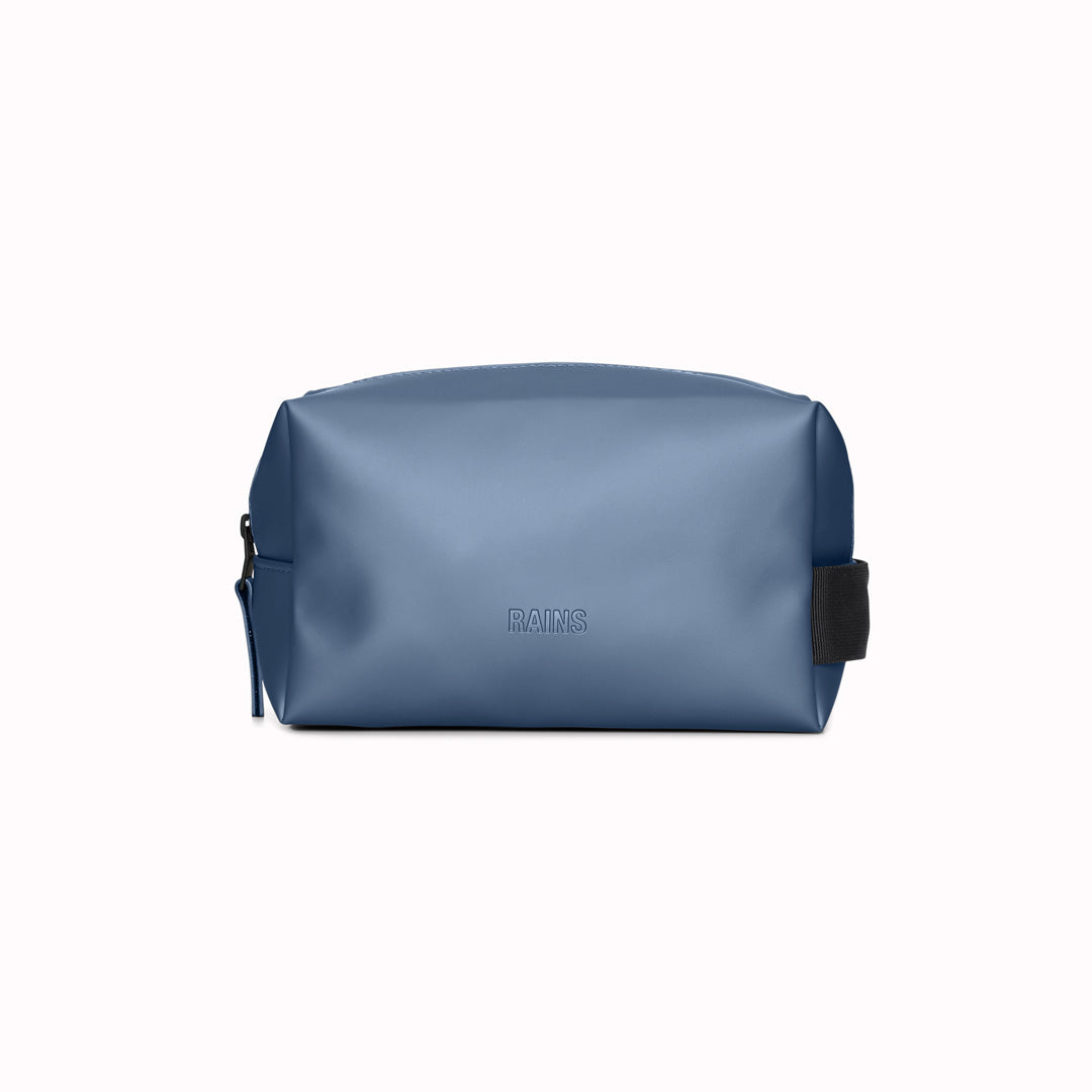 Side View - SS24 collection Wash Bag by Rains in Earth. A unisex wash bag by Rains&nbsp;featuring one main compartment with inside sleeve pockets and is large enough to fit one’s essential toiletries. Made from a smooth, waterproof fabric&nbsp;it also&nbsp;has a webbing grab handle and a water-repellent zipper.