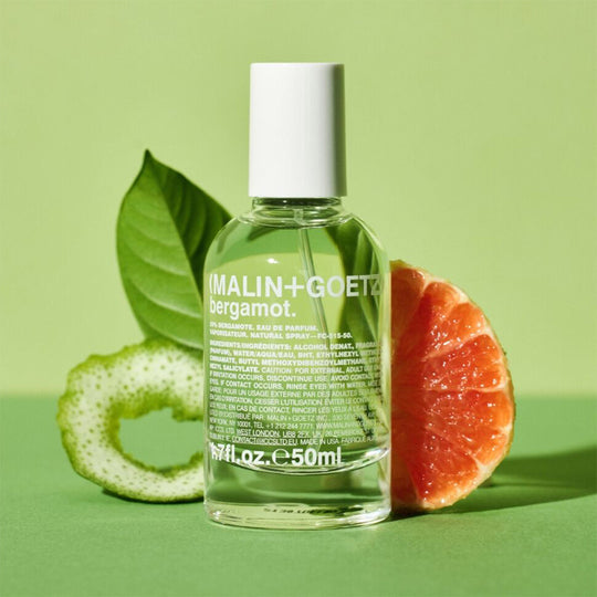 MALIN+GOETZ bergamot perfume bottle with green leaves and a sliced grapefruit on a green background