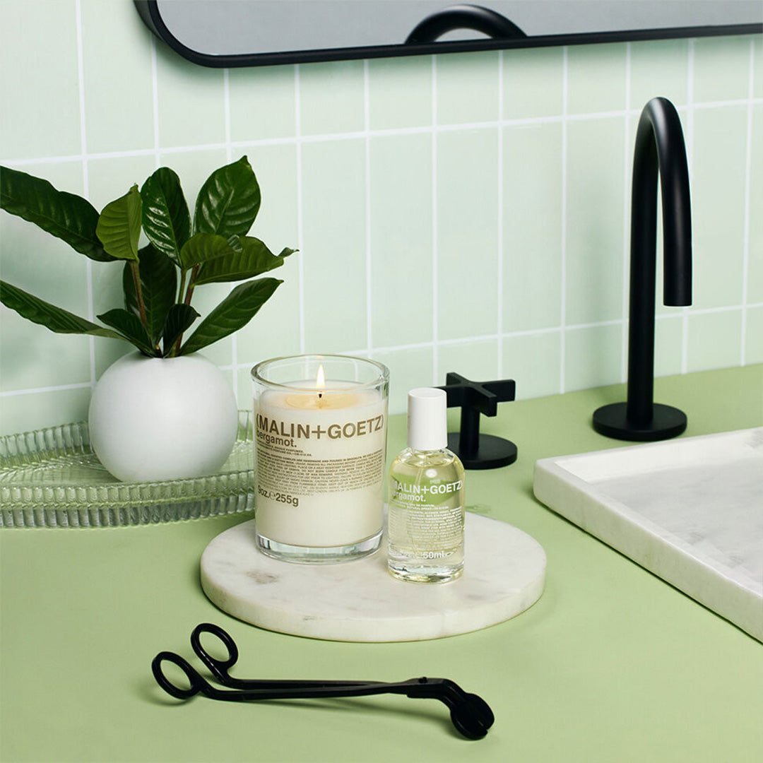 Bathroom counter with Malin+Goetz Bergamot candle, perfume bottle and a plant.
