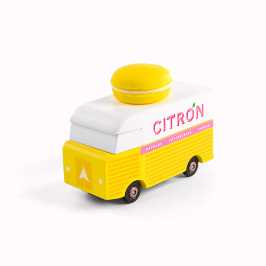 Angled picture of Citron Macaron Van by Candylab. It is a toy vehicle inspired by French pastry shops. It has a bright yellow color and a macaron-shaped roof rack. The van is made of solid beech wood. It is a fun and stylish addition to any child's collection.