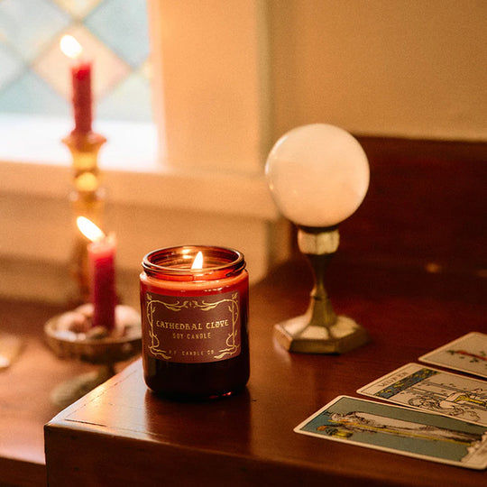 The Cathedral Clove candle from P.F. Candle Co. captures glowing fireplace embers, steam swirling off spiced tea, cool night air weaving through lace drapes.