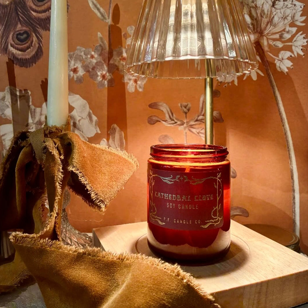 The Cathedral Clove candle from P.F. Candle Co. captures glowing fireplace embers, steam swirling off spiced tea, cool night air weaving through lace drapes.