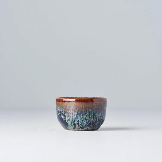 Lifestyle Image - Brown Black Sake Cup with blue drip glaze from Made in Japan. Working from the dark base, the blue is applied to the rim from above and allowed to drip down the cup to create an organic look.