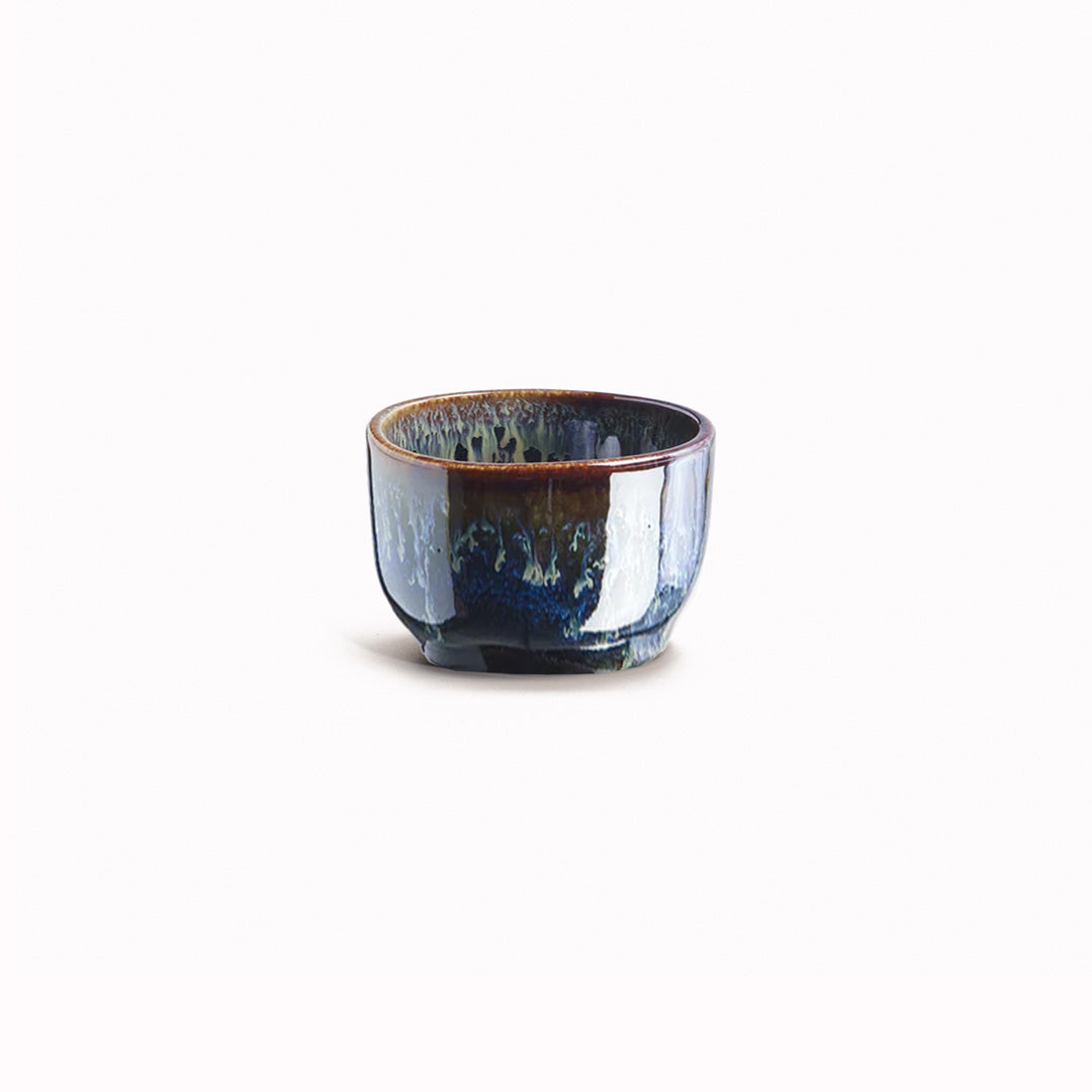 Brown Black Sake Cup with blue drip glaze from Made in Japan. Working from the dark base, the blue is applied to the rim from above and allowed to drip down the cup to create an organic look.