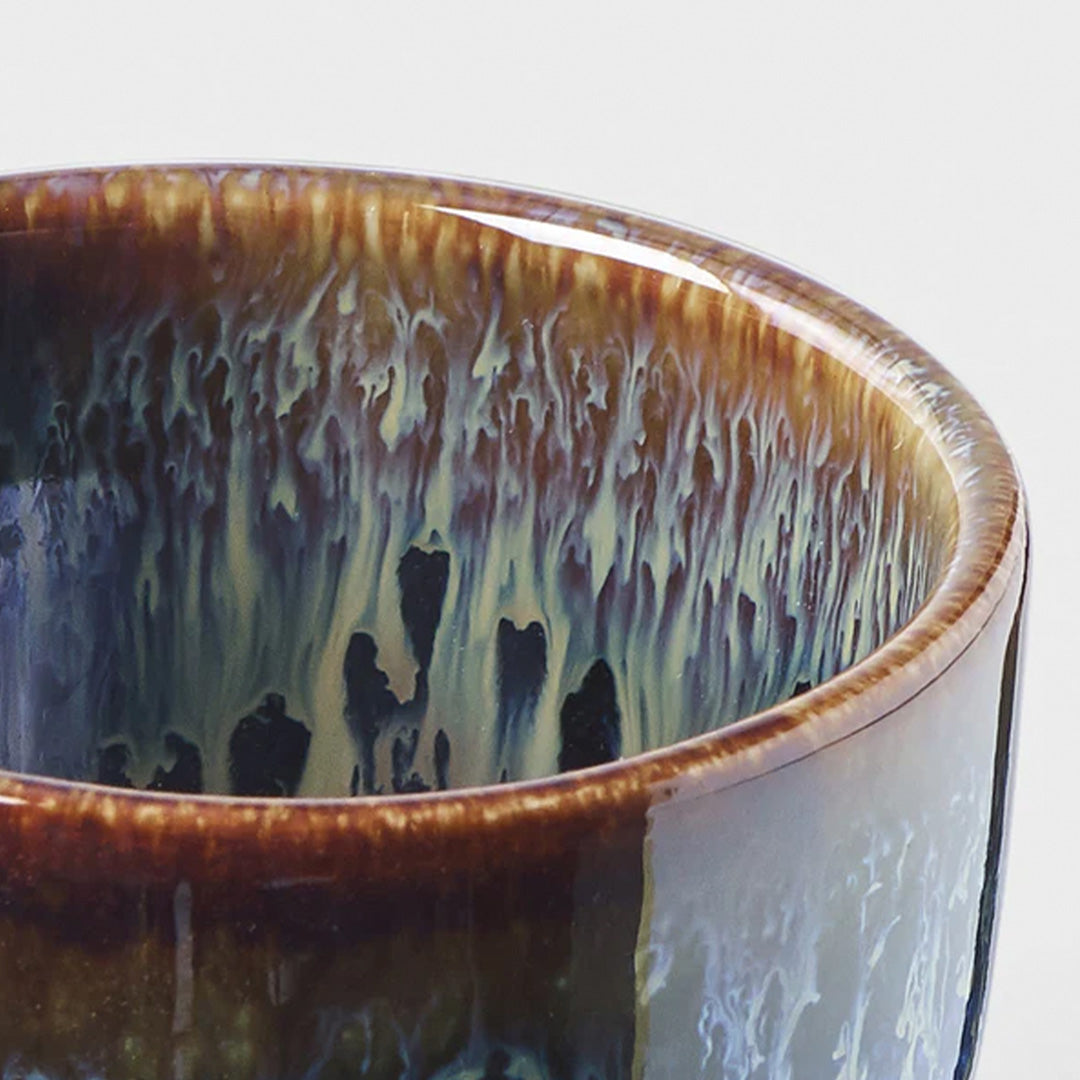 Detail Close Up - Brown Black Sake Cup with blue drip glaze from Made in Japan. Working from the dark base, the blue is applied to the rim from above and allowed to drip down the cup to create an organic look.