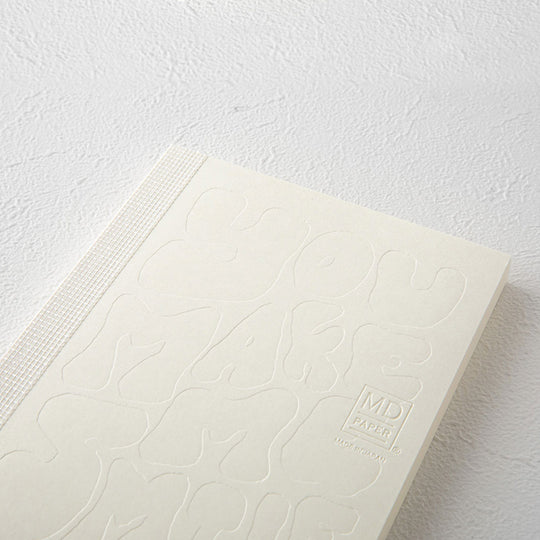 This A6 plain paper notebook has an off white cover embossed with some ace artwork by Charlene Man featuring the words 'You Make Me Smile' in a hand-typography style. The MD paper logo is also embossed. 