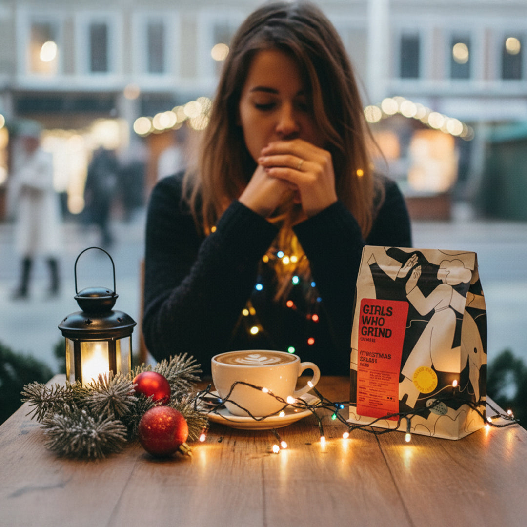 Woman sitting at a table with a cup of coffee, decorative lantern, and 'Girls Who Grind' coffee bag.