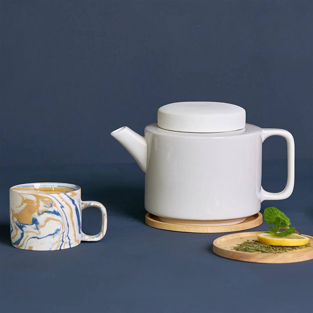 Lifestyle image of blue and mustard marbled gloss glaze mug from Dutch company Kinta, who produce contemporary ceramics and homeware. The stoneware mug has a striking marbled effect glaze with blue and mustard colouring. The glaze on the outside and on the interior is glossy and it holds 200ml