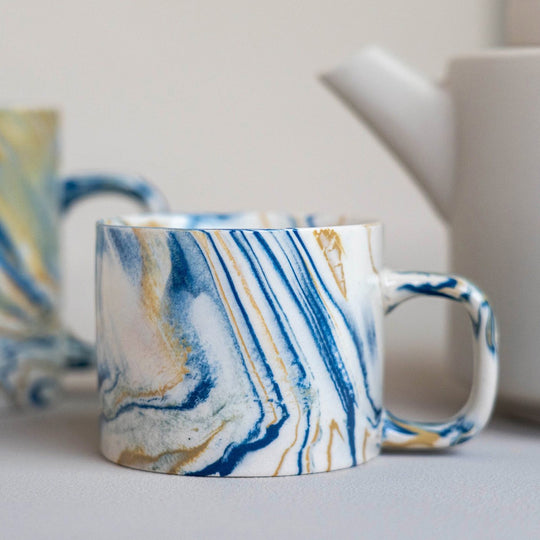 Detail of blue and mustard marbled gloss glaze mug from Dutch company Kinta, who produce contemporary ceramics and homeware. The stoneware mug has a striking marbled effect glaze with blue and mustard colouring. The glaze on the outside and on the interior is glossy and it holds 200ml