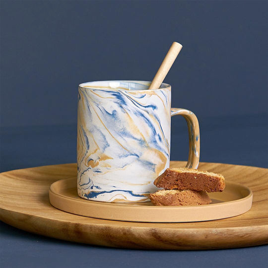 Lifestyle Image - blue and mustard marbled gloss glaze mug from Dutch company Kinta, who produce contemporary ceramics and homeware. The stoneware mug has a striking marbled effect glaze with blue and mustard colouring. The glaze on the outside and on the interior is glossy and it holds 350ml
