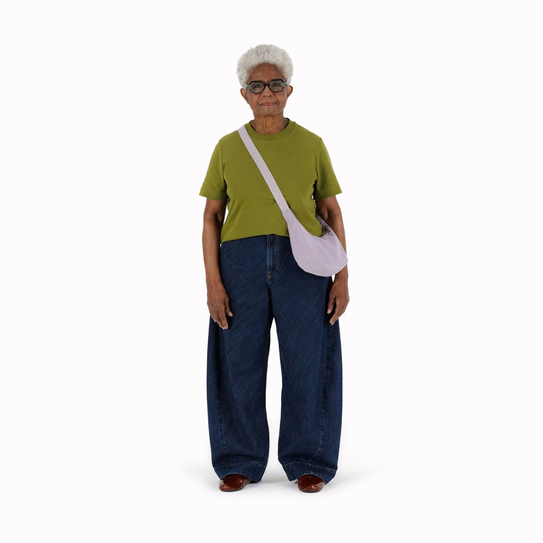 It is made of durable nylon and features a zippered main compartment, an interior slip pocket with integrated keyleash, and an adjustable shoulder strap. The bag has a curved shape that hugs your body and a sleek design that adds a touch of elegance
