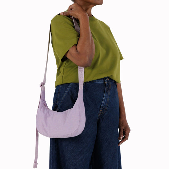 It is made of durable nylon and features a zippered main compartment, an interior slip pocket with integrated keyleash, and an adjustable shoulder strap. The bag has a curved shape that hugs your body and a sleek design that adds a touch of elegance