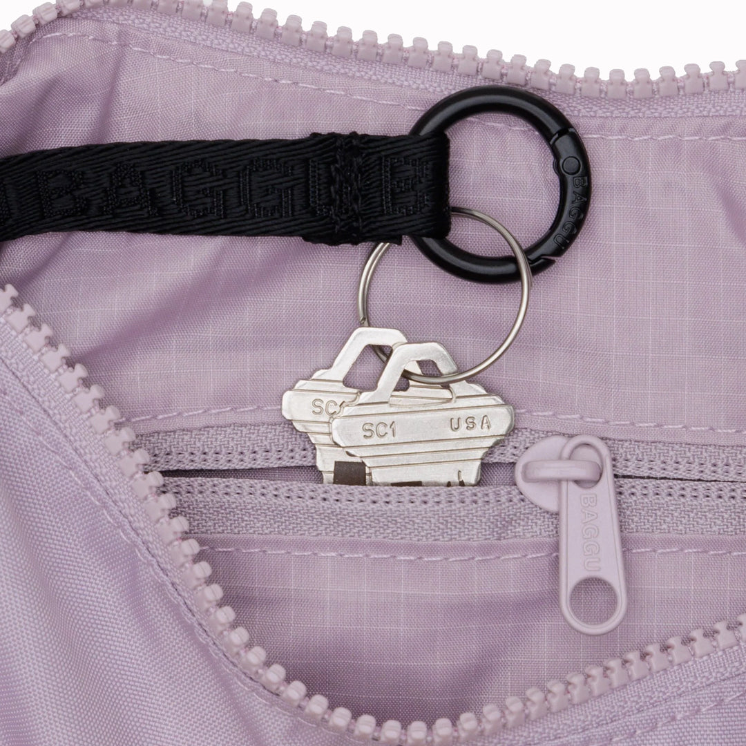 It is made of durable nylon and features a zippered main compartment, an interior slip pocket with integrated keyleash, and an adjustable shoulder strap. The bag has a curved shape that hugs your body and a sleek design that adds a touch of elegance