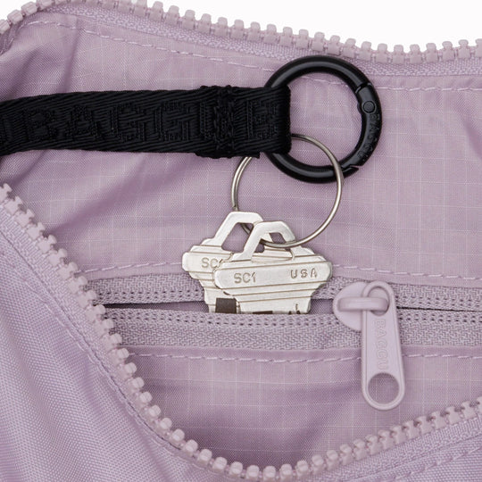 It is made of durable nylon and features a zippered main compartment, an interior slip pocket with integrated keyleash, and an adjustable shoulder strap. The bag has a curved shape that hugs your body and a sleek design that adds a touch of elegance