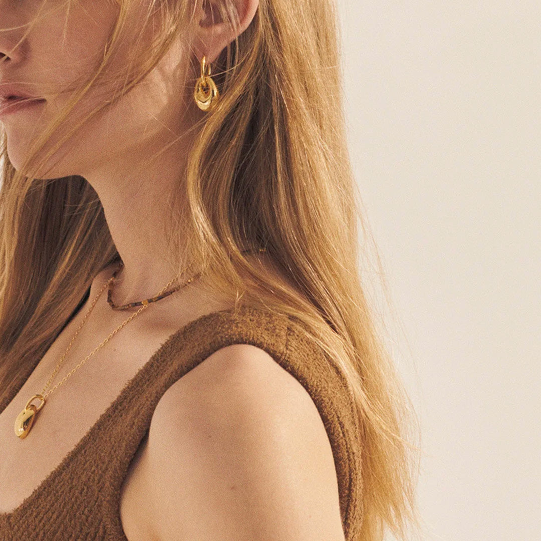 The Anni Lu Golden Pebble Earrings are a stunning addition to any collection, inspired by the natural beauty of Pebble Beach's rounded stones. These earrings are crafted from 18kt gold-plated brass and feature an anti-tarnish e-coating, ensuring their lustre lasts.