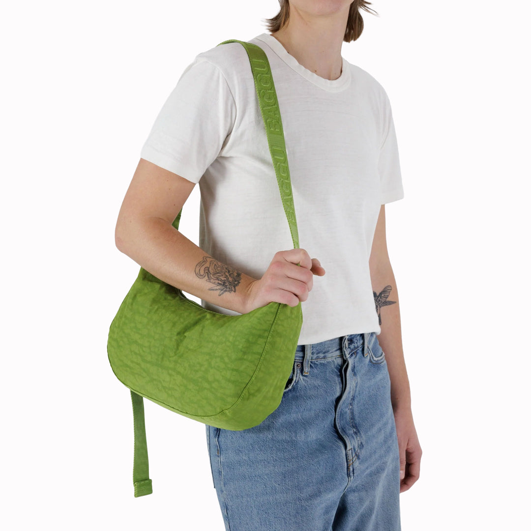 The Medium Crescent Bag in Green Juice from Baggu is a stylish and versatile accessory that can complement any outfit. It is made of durable nylon and features a zippered main compartment, an interior slip pocket, and an adjustable shoulder strap.
