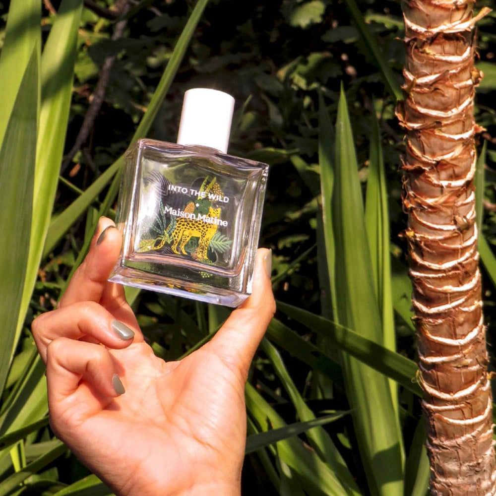 Maison Matine's 'Into the Wild' is a scent inspired by nature, travel and life's adventures, all housed in an illustrative glass bottle. 50ml bottle in models hand.
