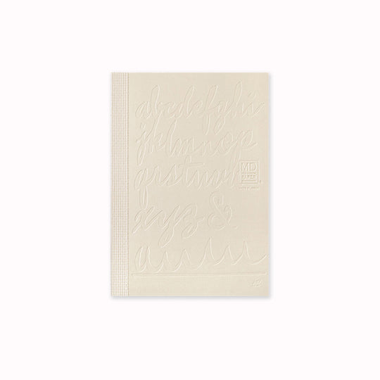 Unwrapped, This A6 plain paper notebook has an off white cover embossed with some ace artwork by Kenji Nakayama featuring a calligraphic alphabet. The MD paper logo is also embossed.  