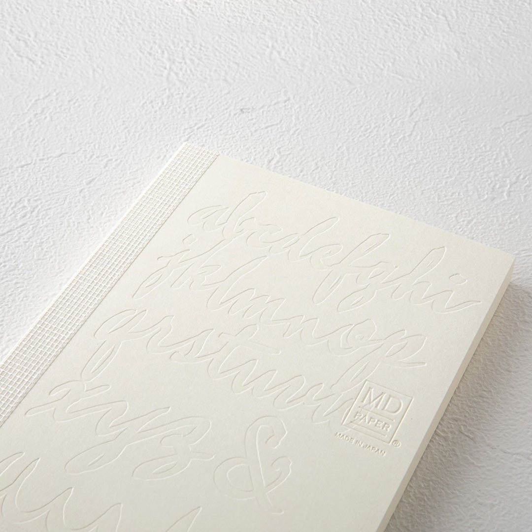 Detail of shis A6 plain paper notebook has an off white cover embossed with some ace artwork by Kenji Nakayama featuring a calligraphic alphabet. The MD paper logo is also embossed.  