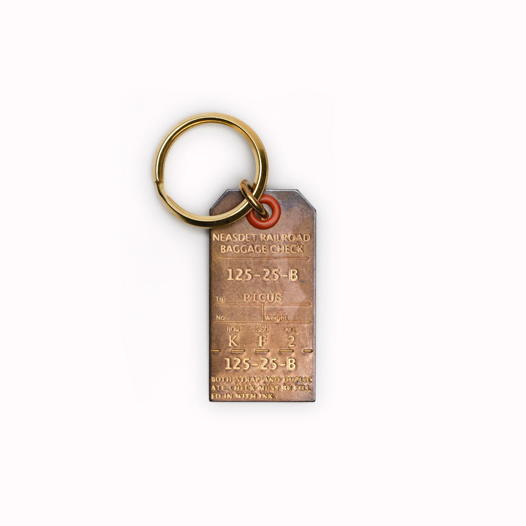 A small Japanese keychain from Picus designed to resemble an antique luggage tag and made from a stamped solid brass with an aged finish.