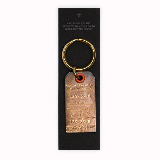 A small Japanese keychain from Picus designed to resemble an antique luggage tag and made from a stamped solid brass with an aged finish.