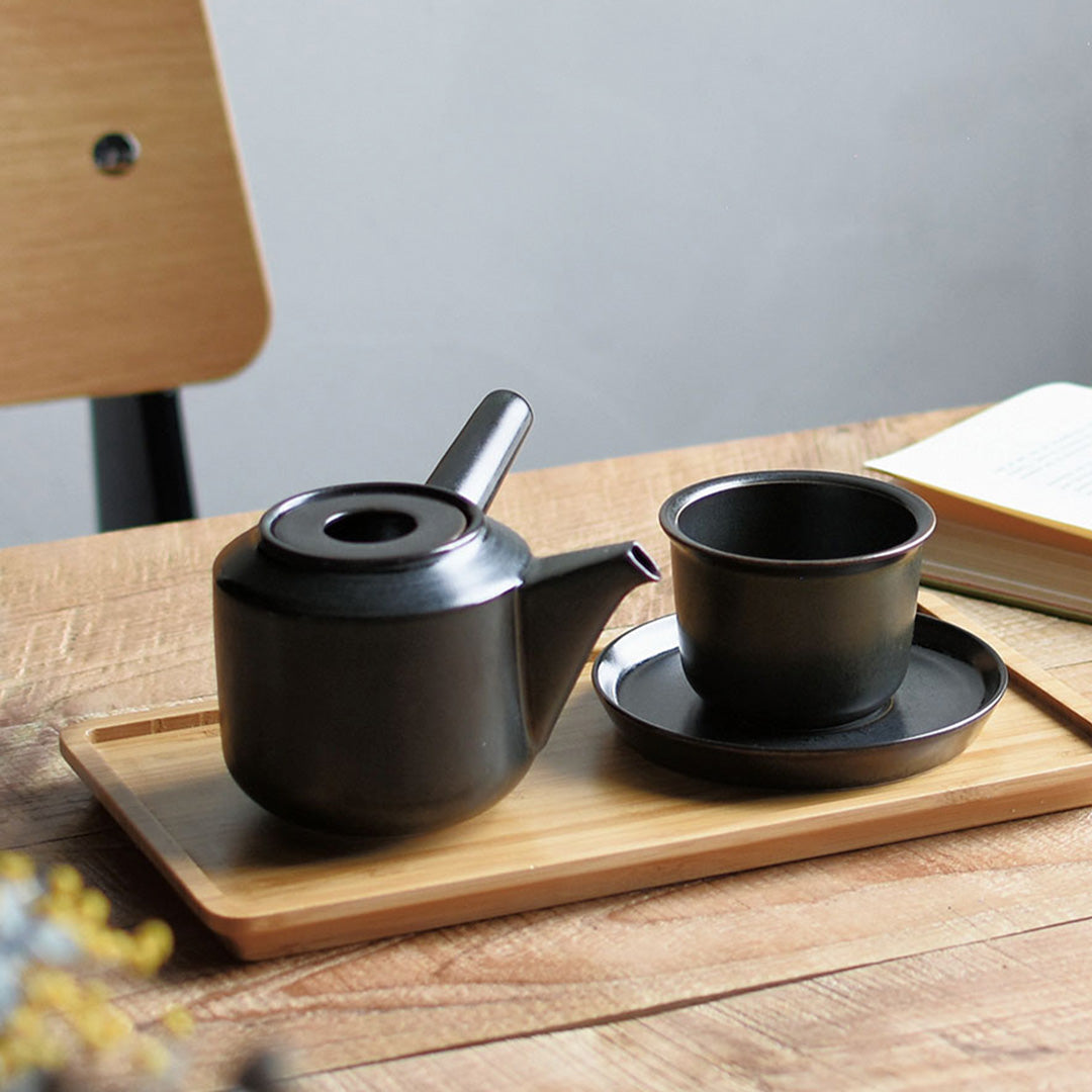 Lifestyle shot, with cup. The Leaves to Tea teapot from Kinto is made of black porcelain, and features a sleek design that blends well with any tableware. The teapot has a large side handle that is easy to grip and a spout that pours smoothly.  It holds 300ml and is perfect for making a single cup of tea.