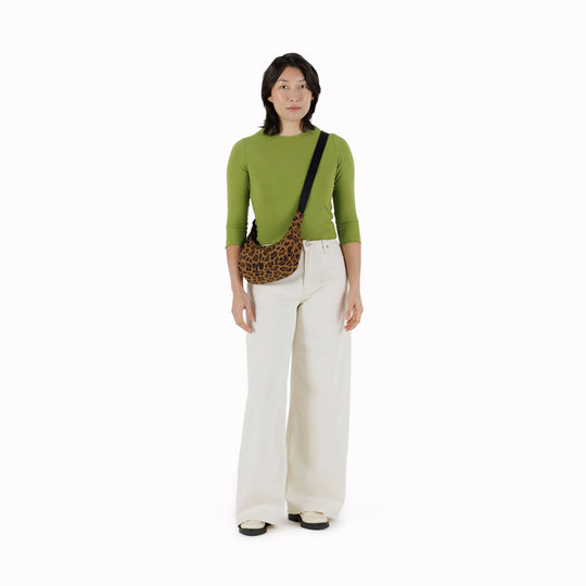It is made of durable nylon and features a zippered main compartment, an interior slip pocket with integrated keyleash, and an adjustable shoulder strap. The bag has a curved shape that hugs your body and a sleek design that adds a touch of elegance