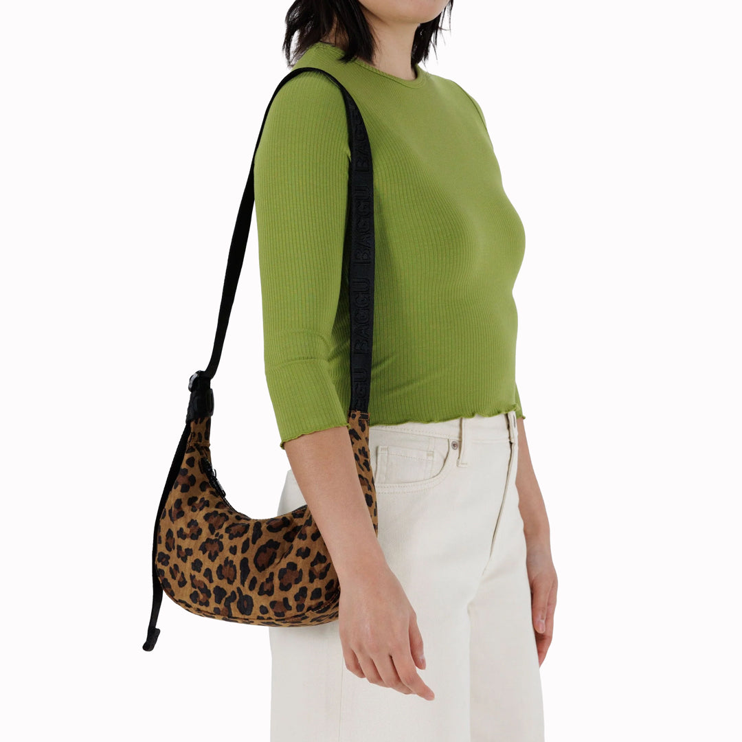It is made of durable nylon and features a zippered main compartment, an interior slip pocket with integrated keyleash, and an adjustable shoulder strap. The bag has a curved shape that hugs your body and a sleek design that adds a touch of elegance
