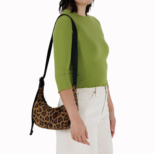 It is made of durable nylon and features a zippered main compartment, an interior slip pocket with integrated keyleash, and an adjustable shoulder strap. The bag has a curved shape that hugs your body and a sleek design that adds a touch of elegance