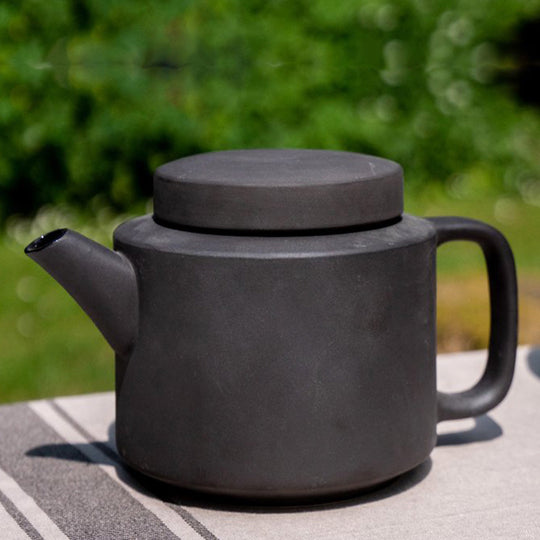 Lifestyle image of large stoneware teapot from Dutch company Kinta who produce contemporary ceramics and homeware. The large teapot is black, with a soft matt exterior finish. Its design is influenced  by ceramic trends of the 1960s, but with a pleasing modern and neutral colour palette.