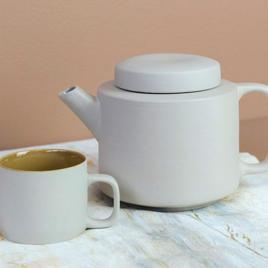 Lifestyle image with cup of the extra large stoneware teapot from Dutch company Kinta who produce contemporary ceramics and homeware. The extra large teapot is clay grey in colour, with a soft matt exterior finish. Its design is influenced  by ceramic trends of the 1960s, but with a pleasing modern and neutral colour palette. 