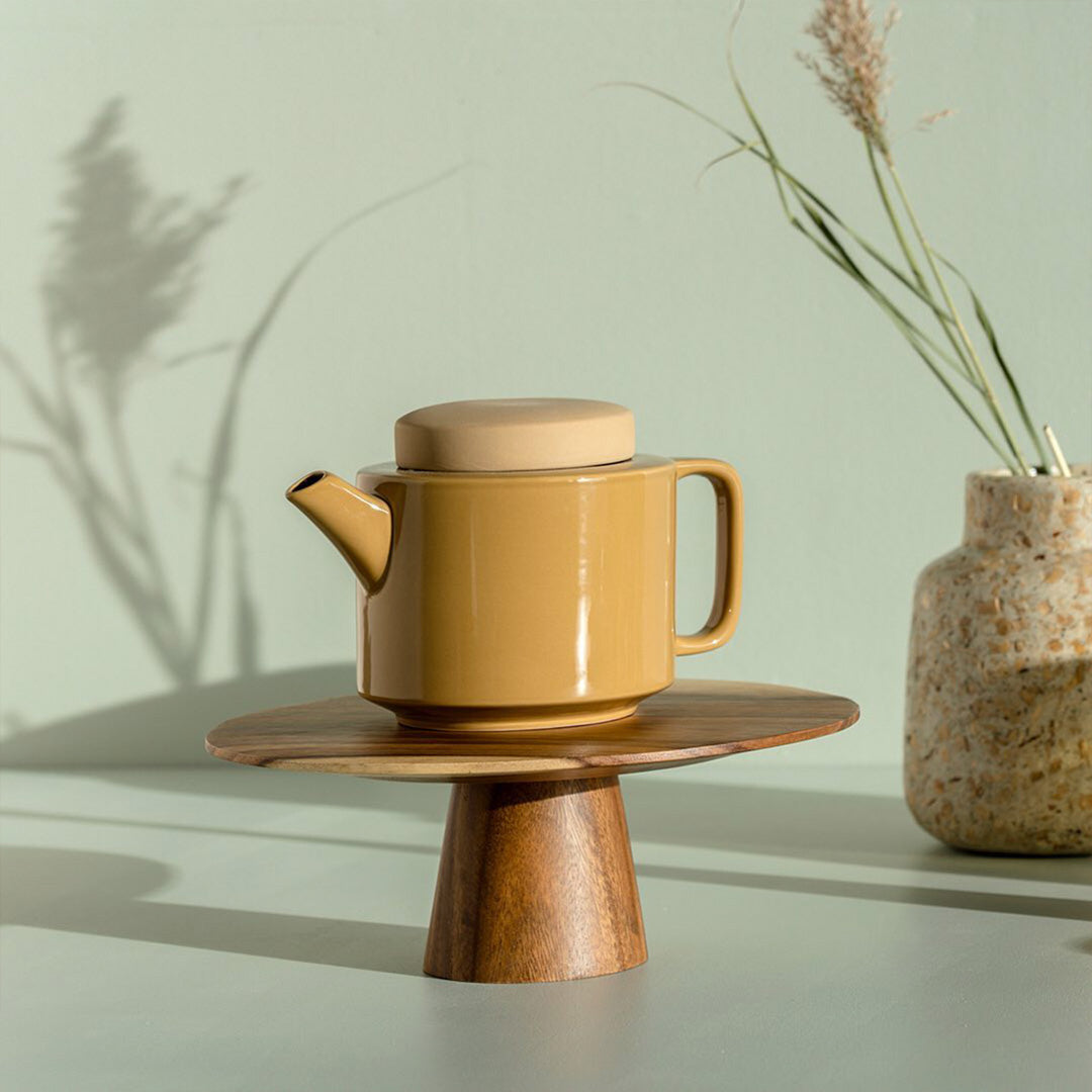 on a plinth, a small stoneware teapot from Dutch company Kinta who produce contemporary ceramics and homeware. The small size teapot is mustard yellow, with a gloss glaze exterior body finish and matt glaze lid. Its design is influenced  by ceramic trends of the 1960s, but with a pleasing modern and neutral colour palette.