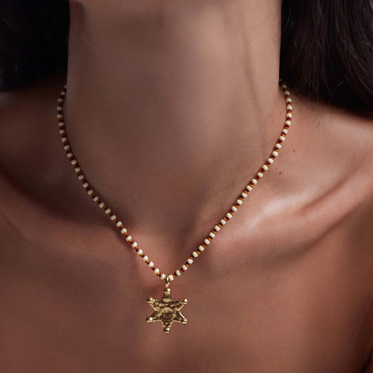 he Anni Lu Lucky Star necklace is a gold Western inspired star shaped gold pendant with glass beaded necklace chain in neutral hazel brown, rust and ecru colours.