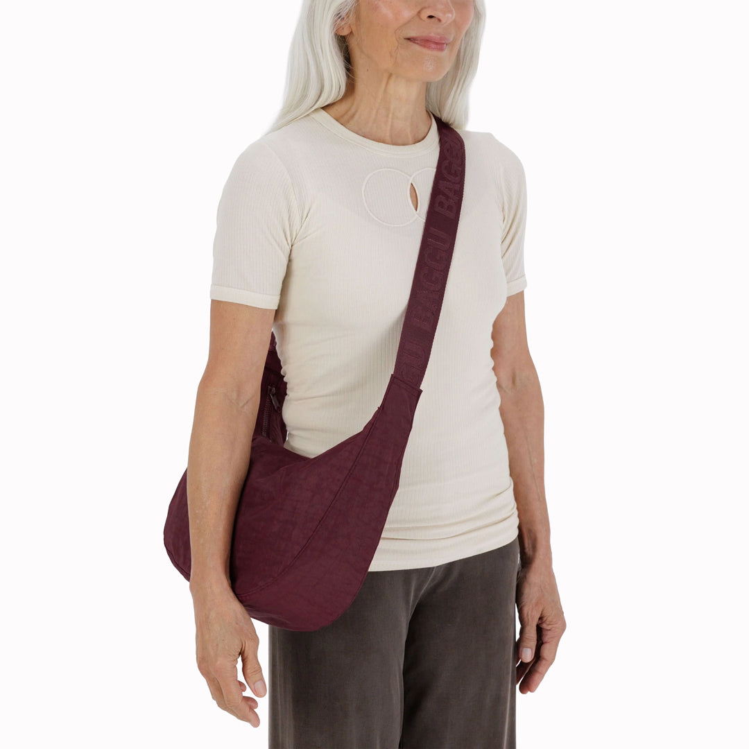 The Medium Crescent Bag in Mahogany from Baggu is a stylish and versatile accessory that can complement any outfit. It is made of durable nylon and features a zippered main compartment, an interior slip pocket, and an adjustable shoulder strap.