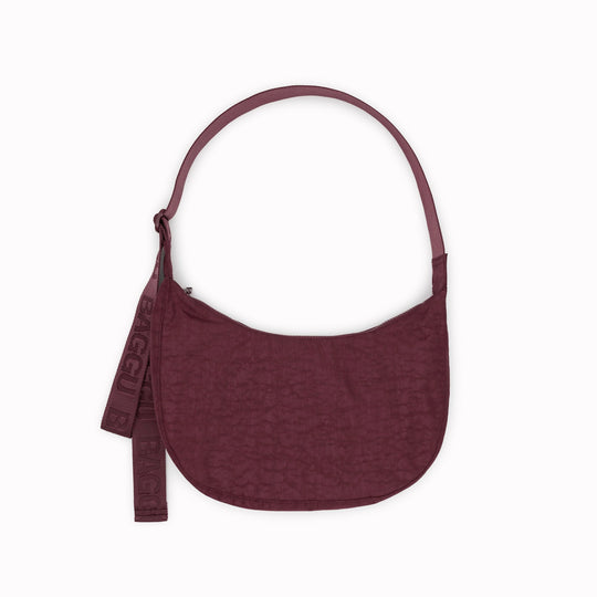 The Medium Crescent Bag in Mahogany from Baggu is a stylish and versatile accessory that can complement any outfit. It is made of durable nylon and features a zippered main compartment, an interior slip pocket, and an adjustable shoulder strap.